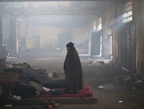 Un homme se trouve au milieu de l'entrepôt utilisée comme abri par des réfugiés à Belgrade © Marko Drobnjakovic. Serbie, 2017.